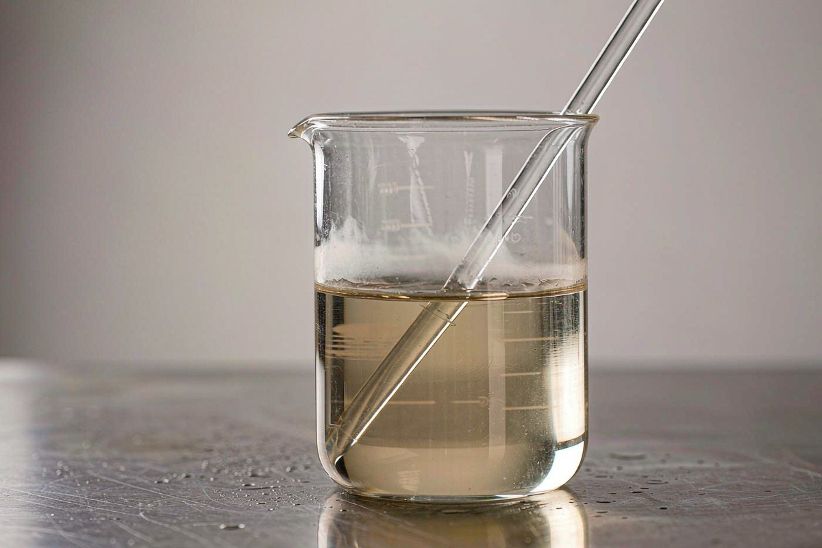 glass beaker of pale yellowish brown cardanol diglycidyl ether YLD-9016 on a brushed stainless laboratory bench