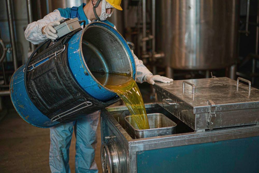 worker decanting warm amber novolac epoxy resin from a heater-jacketed steel drum into a stainless impregnation bath
